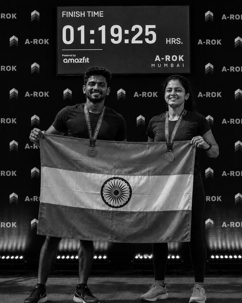 Two A-ROK Mumbai finishers standing composed with their medals under a finish clock reading 01:19:25
